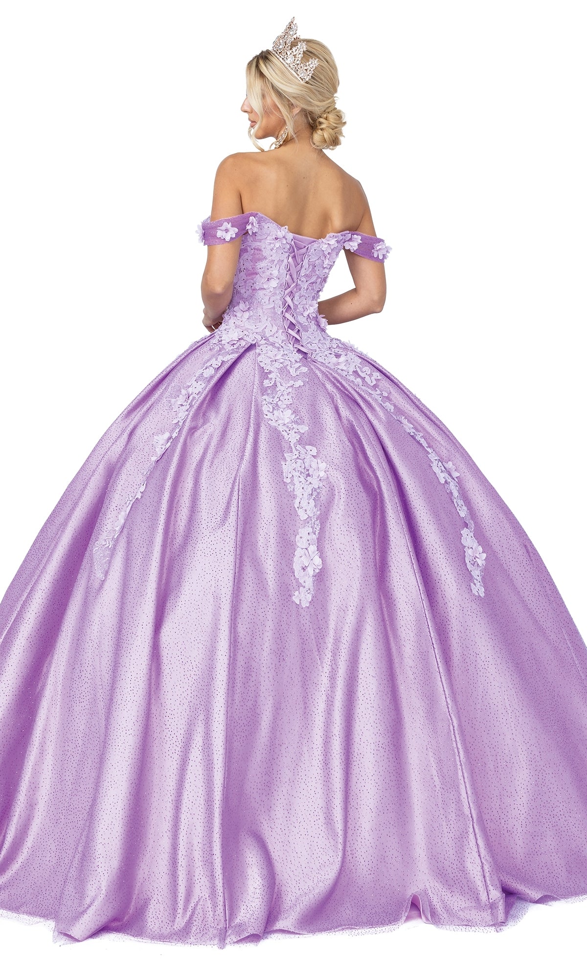 A woman wearing a tiara and the Quinceanera Dress 1501 by Dancing Queen—a floor-length, lavender a-line ball gown with lace details and off-the-shoulder sleeves—stands facing away.